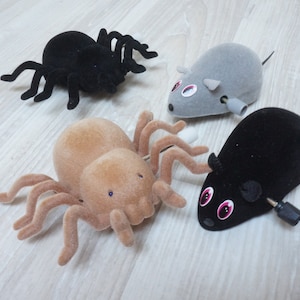 Puede incluir: Cuatro juguetes de cuerda: una araña negra, una araña marrón, un ratón gris y un ratón negro. Los ratones tienen ojos rojos y las arañas tienen ojos negros.