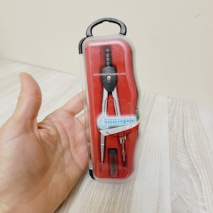 May include: A red and clear plastic case containing a silver compass. The case has a black handle and the compass has the word "ecnocompass" printed on it.