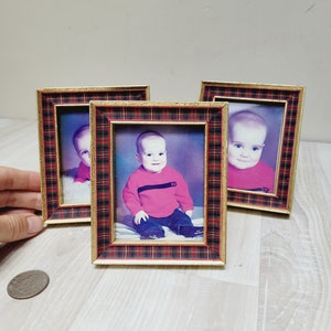 May include: Three small picture frames with gold trim and a red and black plaid design. Each frame contains a photo of a young child wearing a red shirt.