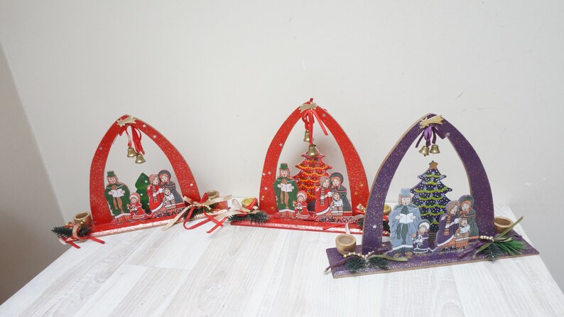 K&ouml;nnte beinhalten: Drei Weihnachtsdekorationen aus Holz mit einer Weihnachtskrippe und einem Weihnachtsbaum. Die Dekorationen sind in Rot, Lila und Gr&uuml;n bemalt. Jede Dekoration hat zwei Kerzenhalter.