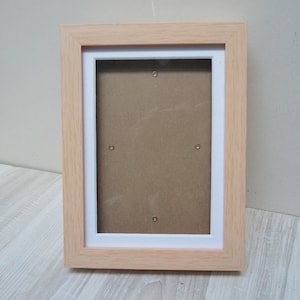 May include: A natural wood picture frame with a white mat and a brown backing. The frame is empty and ready for a photo.