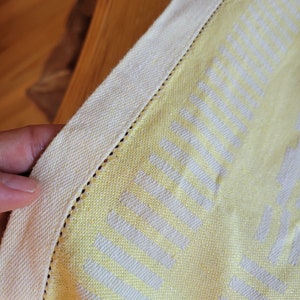 May include: A yellow and white woven tablecloth with a white border. The tablecloth has a repeating pattern of white vertical lines.