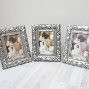 Op de afbeelding: Drie zilveren fotolijsten met sierlijke ontwerpen, elk met een zwart-witfoto van een vrouw met donker haar.