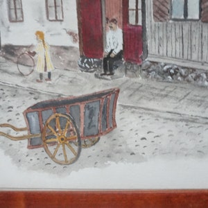 May include: Watercolor painting of a street scene with a child holding a hoop, a man sitting on a porch, and a wooden cart. The artwork is framed in a brown wooden frame. The painting has a vintage aesthetic.