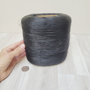 May include: A large spool of black thread, wound tightly and ready for use. The spool is sitting on a light wood surface.