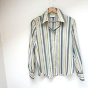 Puede incluir: Una camisa de manga larga con botones y rayas verticales en tonos de verde, amarillo y blanco.