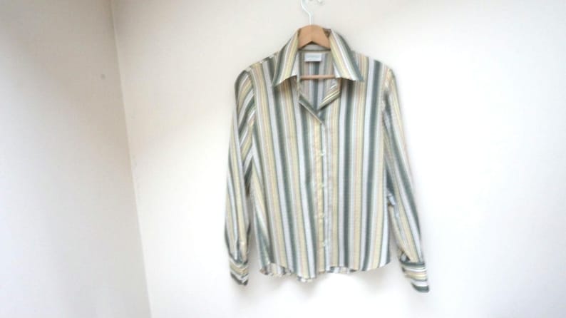 Puede incluir: Una camisa de manga larga con botones y rayas verticales en tonos de verde, amarillo y blanco.