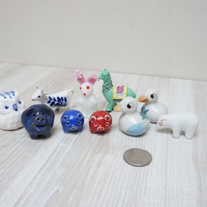 May include: A collection of 10 small ceramic figurines of various animals, including a pig, a rabbit, a duck, a llama, and an owl. The figurines are painted in white, blue, red, and green.