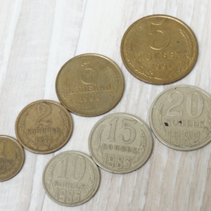 Könnte beinhalten: Eine Sammlung von sechs alten sowjetischen Münzen mit den Nennwerten 1, 2, 5, 10, 15 und 20 Kopeken. Die Münzen sind in einer Reihe vom kleinsten zum größten angeordnet, wobei die 1-Kopeken-Münze links und die 20-Kopeken-Münze rechts liegt. Alle Münzen sind aus Kupfer und haben ein leicht abgenutztes Aussehen.