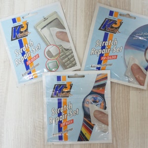 May include: Three packs of scratch repair kits for different surfaces. The packs are white with blue and red accents. The text on the packs reads "Scratch Repair-Set" and specifies the surface the kit is for: "For Display", "For CD/DVD", and "For Watch".