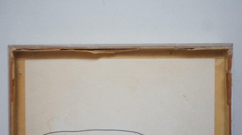 May include: A framed artwork with a white background and a thin black line drawing in the center. The frame is made of wood and has a light brown color. The frame is slightly damaged on the top edge.