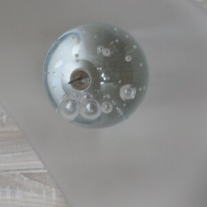 May include: A clear glass sphere with small air bubbles inside. The sphere is sitting on a white surface.