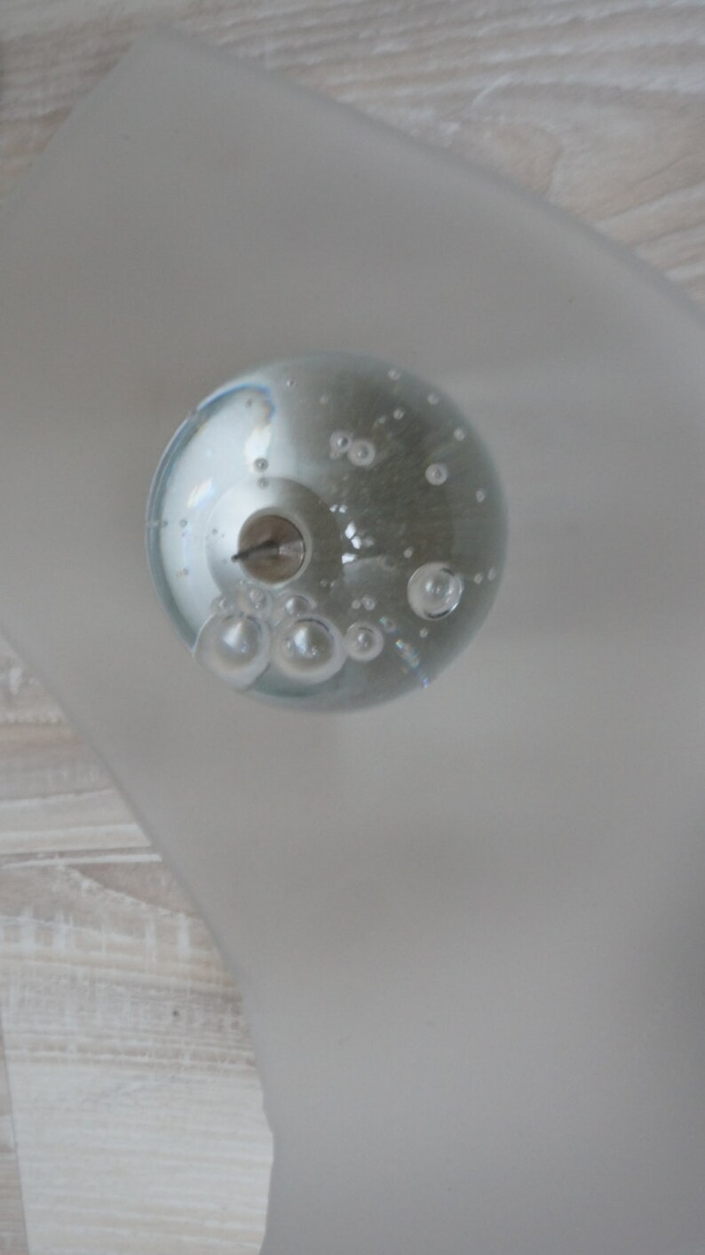 May include: A clear glass sphere with small air bubbles inside. The sphere is sitting on a white surface.