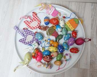 Puede incluir: Un plato blanco lleno de decoraciones de Pascua coloridas, incluyendo huevos de madera, pollitos, conejos y algunas decoraciones de tela.
