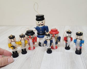 May include: A set of eight wooden nutcracker ornaments. The ornaments are painted in various colors, including red, blue, yellow, and white. The nutcrackers have white beards and black hats.
