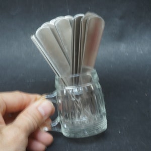 K&ouml;nnte beinhalten: Ein durchsichtiger Glasbecher mit Henkel, der eine Gruppe silberner L&ouml;ffel h&auml;lt.