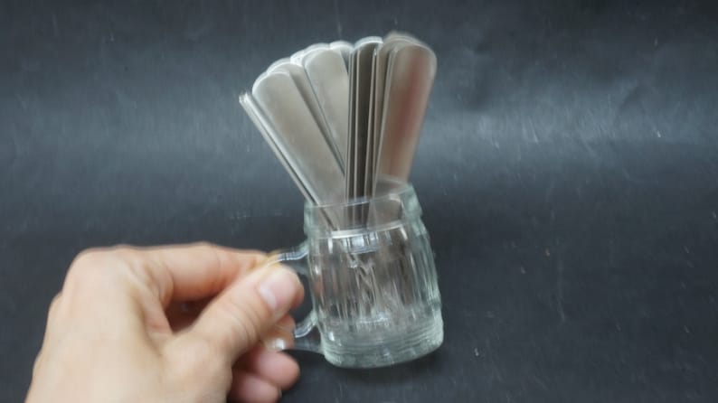 K&ouml;nnte beinhalten: Ein durchsichtiger Glasbecher mit Henkel, der eine Gruppe silberner L&ouml;ffel h&auml;lt.