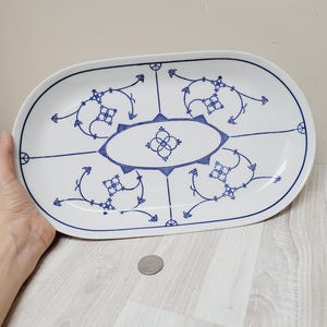 May include: A white oval serving platter with a blue and white floral design. The design features a central oval with a repeating pattern of four circles and a cross.