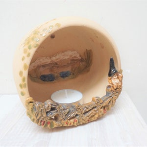 May include: A ceramic candle holder shaped like a half-sphere with a small candle inside. The holder is decorated with a scene of a house and a pond, and the bottom edge is decorated with a row of small figures.