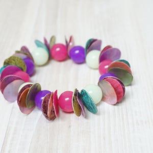 May include: A colorful bracelet made of layered, iridescent, shell-like beads in shades of pink, purple, green, and white.