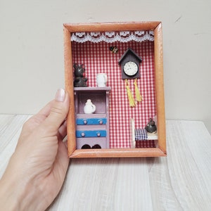 May include: A miniature wooden diorama with a red and white checkered background. The diorama features a small wooden house with a purple door and blue trim, a clock with yellow tassels, a small black mouse figurine, and a white mug.