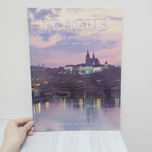 Pode incluir: Um livro intitulado "PRAGUE and its history" com uma imagem de Praga ao entardecer. A capa inclui texto em inglês, alemão e francês. Os nomes dos autores também são visíveis.