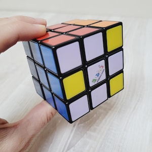 May include: A black and white Rubik's Cube with yellow, red, blue, and purple squares. The cube has the text "Rubik's.com" on one side.