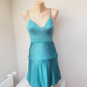 Peut inclure: Une robe de nuit en satin bleu turquoise avec un corsage en dentelle et une jupe fluide. La robe est sur un mannequin et est exposée sur un panier en osier.