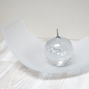 May include: A clear glass orb with a silver top sits on a white frosted curved dish. The orb contains small clear glass bubbles.