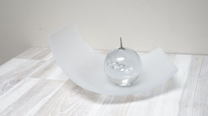 May include: A clear glass orb with a silver top sits on a white frosted curved dish. The orb contains small clear glass bubbles.
