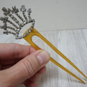 May include: A vintage hair comb with a decorative crown of rhinestones. The comb is made of brown plastic and has two prongs.