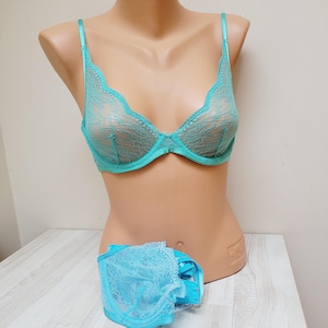 May include: A turquoise lace bra and matching underwear set displayed on a mannequin. The bra features delicate lace detailing and adjustable straps. The underwear is also made of turquoise lace. The set is displayed on a light-colored surface.