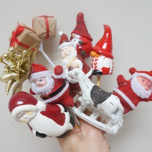 Op de afbeelding: Een verzameling kerstversiering met kerstman, schommelpaard en kabouters. De versiering is gemaakt van keramiek en heeft een vintage uitstraling.