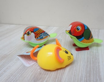 May include: Three colorful wind-up toys: two birds and a mouse. The birds have red, blue, green, and yellow details. The yellow mouse has orange ears and a tail. All toys have green feet.