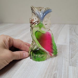 May include: A clear glass owl figurine with a blue and white head, green and pink wings, and a green base. The figurine has the words "Rio Mallorca" on the base.