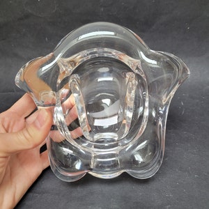 May include: A clear glass bowl with a wavy, organic shape. The bowl is designed with a wide, shallow opening and a rounded bottom.