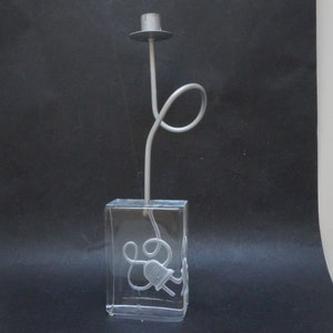 May include: A silver candlestick with a clear glass base. The base has a design of a cord and plug inside.