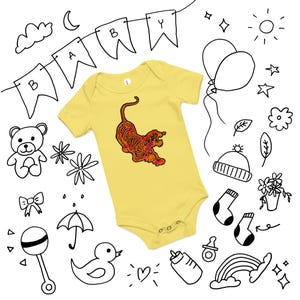 Könnte beinhalten: Gelber Baby-Body mit einem Tiger-Design in Orange- und Rottönen. Das Bild enthält handgezeichnete Illustrationen von Baby-Artikeln, darunter ein Banner mit der Aufschrift "BABY".
