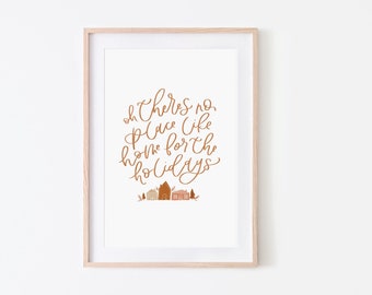 May include: A framed print with the text "Oh there's no place like home for the holidays" in brown cursive script. The print features a small illustration of houses and trees in orange and brown.