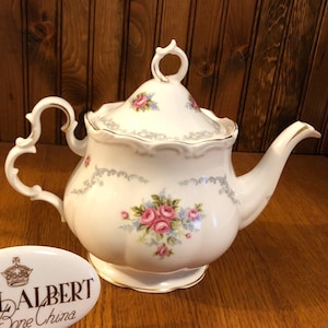 Może przedstawiać: Biały czajnik z kwiatowym wzorem i złotą obwódką. Czajnik został wykonany przez Royal Albert Bone China, Anglia.