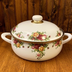 Könnte beinhalten: Weißer Emailletopf mit goldfarbenem Rand und Blumenmuster mit roten, gelben und rosa Rosen. Der Topf hat einen weißen Deckel mit einem goldenen Knopf.