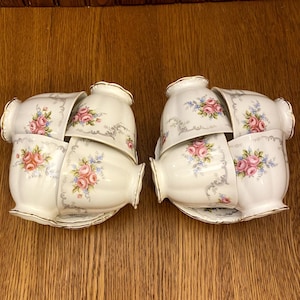 Puede incluir: Seis tazas de té blancas con un patrón floral en tonos de rosa, azul y verde. Las tazas están apiladas en dos grupos de tres, con la taza superior de cada grupo mirando hacia la cámara.