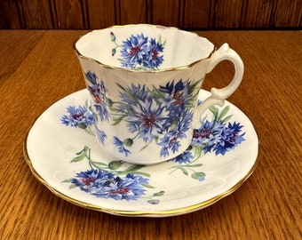 May include: A white teacup and saucer with a blue and white floral pattern. The cup has a gold rim and a handle. The saucer also has a gold rim.