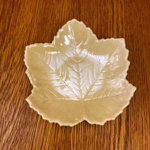 May include: A ceramic leaf-shaped dish in a light beige colour. The dish has a raised design of a leaf with veins.