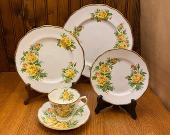 May include: A set of four white porcelain teacups and saucers with a yellow rose floral pattern. The set includes a teacup, saucer, bread and butter plate, and dinner plate.