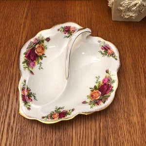 Może przedstawiać: Biała porcelanowa serwetka w kształcie liścia z pozłacanym brzegiem i kwiatowym wzorem. Serwetka ma uchwyt i jest podzielona na dwie części.