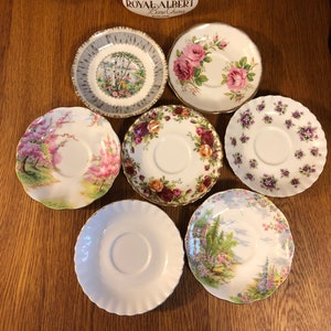 May include: Six Royal Albert Bone China teacups with various floral and landscape designs. The teacups are arranged in a circle on a wooden surface. The label "Royal Albert Bone China England" is visible in the center of the image.