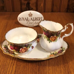 Puede incluir: Un juego de jarra de crema y azucarero de porcelana blanca con un patrón floral, que incluye una bandeja con un borde dorado. El juego es de Royal Albert Bone China, Inglaterra.