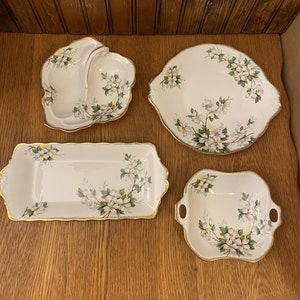 May include: Set of four white porcelain serving dishes with a floral design. The dishes feature a white background with a delicate floral pattern in shades of green and white. The dishes have a gold trim around the edges.