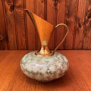 Może przedstawiać: Mały, dekoracyjny dzbanek ceramiczny z mosiężnym dzióbkiem i uchwytem. Dzbanek ma jasnoniebieską podstawę z marmurowym wzorem w odcieniach brązu i zieleni.